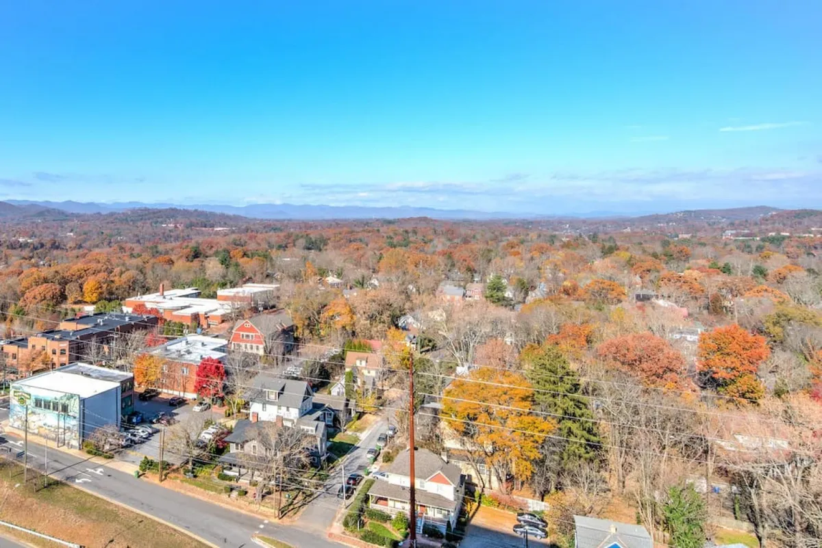 A peaceful cityscape showing colorful autumn trees lining the streets, with small-town buildings and distant mountains in the background. The image conveys the vibrant local neighborhood atmosphere and proximity to Asheville’s downtown, inviting exploration just steps away from the penthouse.