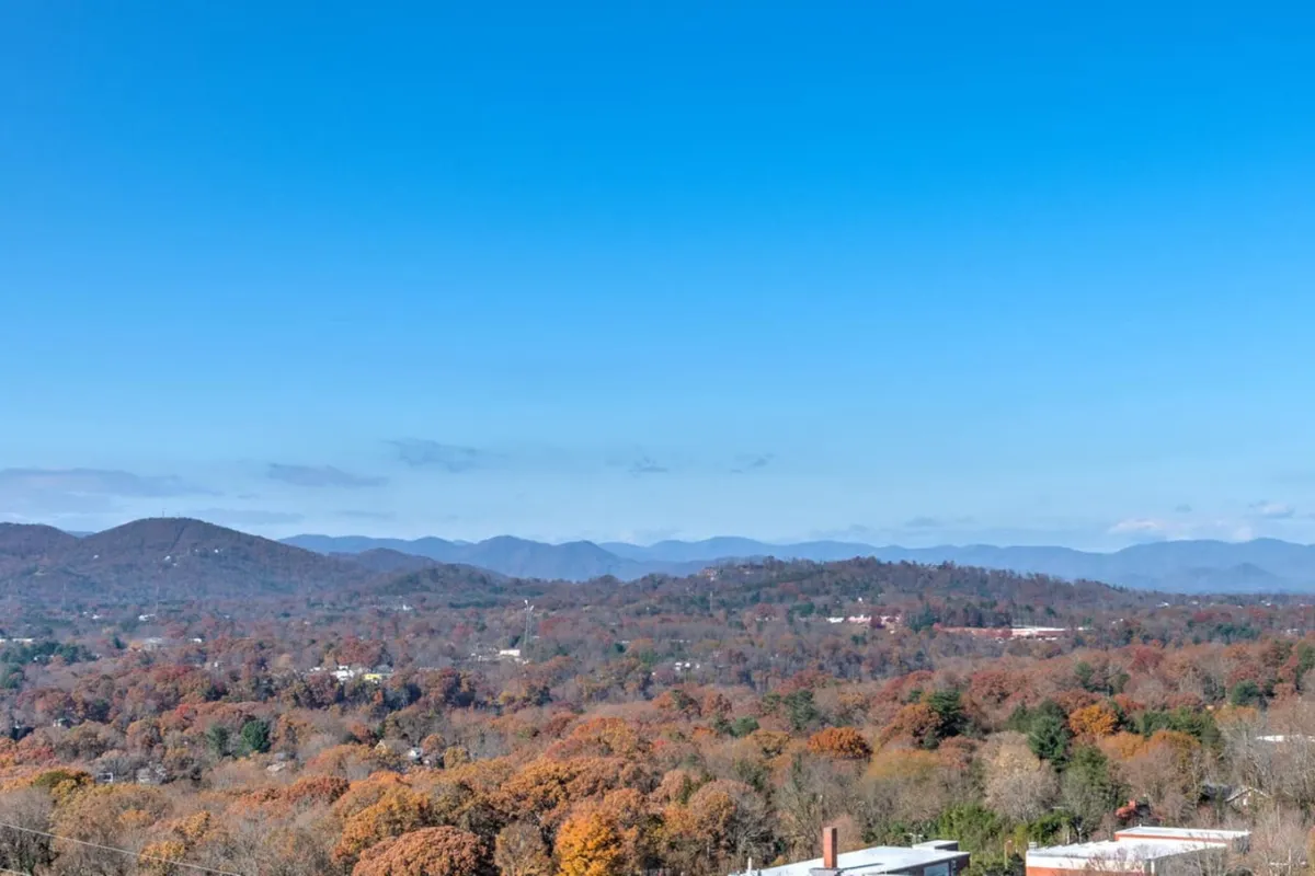 A tranquil, wide-angle view of the Blue Ridge Mountains adorned with colorful fall foliage beneath a clear sky. The untouched natural beauty and soft lighting evoke a sense of peace and possibility, ideal for couples seeking memorable outdoor moments.
