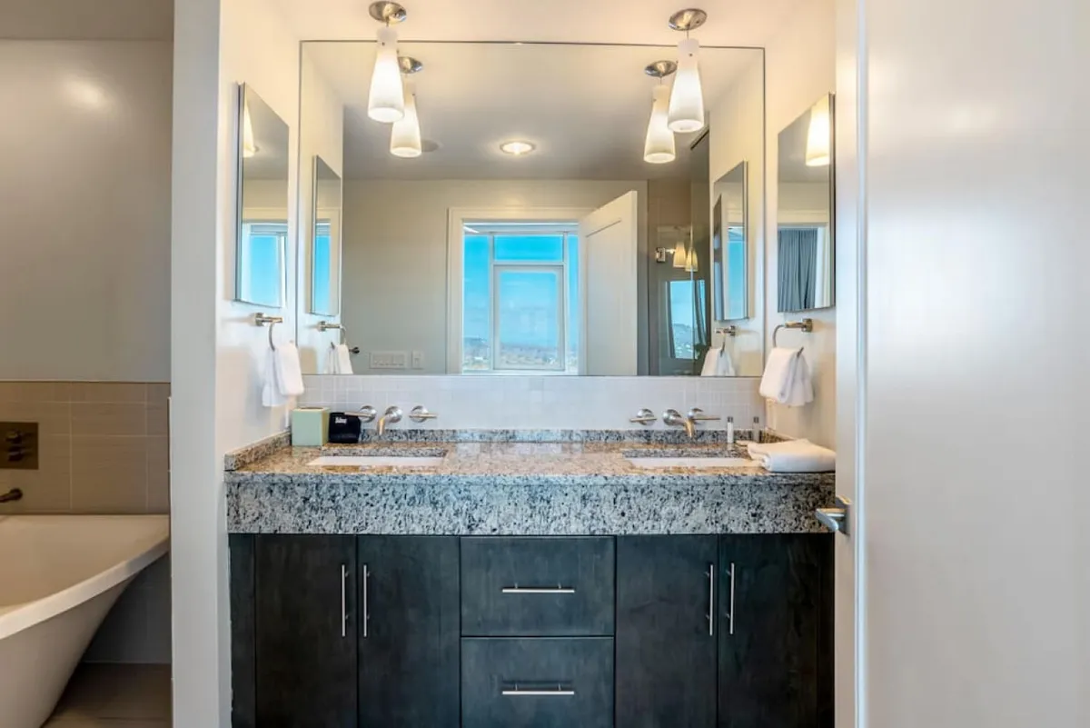 A modern bathroom with a granite countertop, double sinks, large mirrors, and a window offering natural light and a pleasant view. The space feels calm and refreshing, ideally suited to morning routines or post-adventure relaxation.