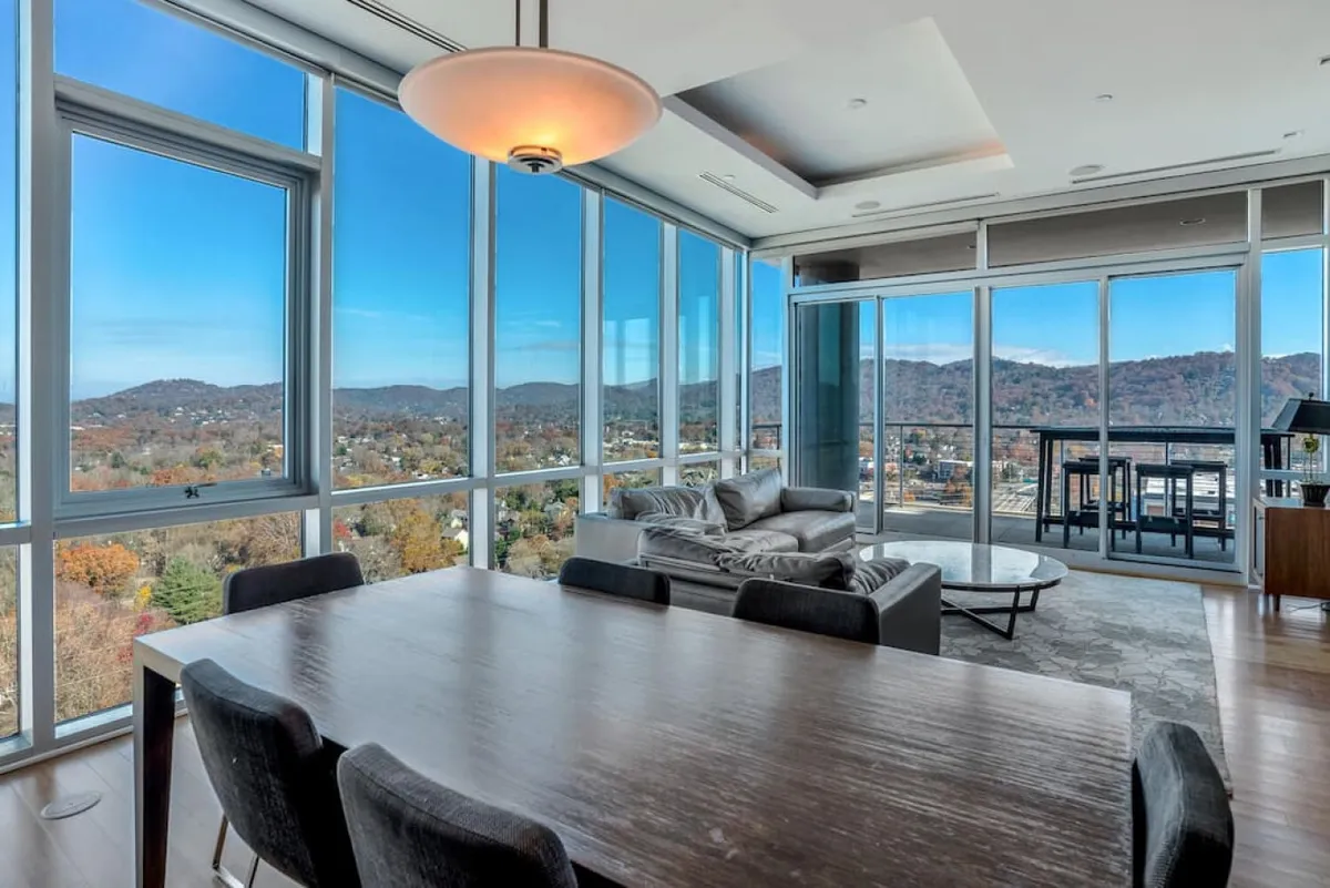 An inviting modern dining and living space with large windows framing the mountain views. Comfortable seating and a dining table offer a seamless transition from indoor elegance to the outdoor experience just beyond the glass.