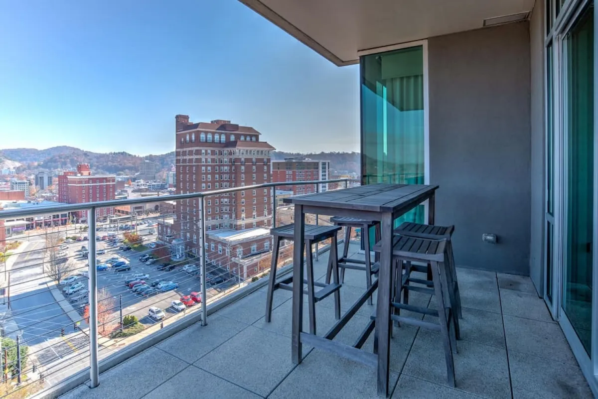 A contemporary private terrace with an outdoor dining table and stool seating, set against an urban Asheville backdrop. The terrace is elevated, offering an inviting spot for morning coffee or sunset cocktails while soaking in city views.
